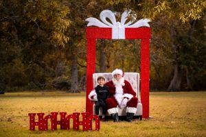 A large red gift box display setup outdoors with holiday decorations in a grassy field with autumn trees in background.