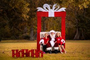 Large red Christmas gift frame prop with white bow sits on autumn grass for festive holiday photos.