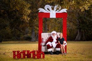 Large red Christmas photo frame setup outdoors with Santa and holiday decorations on autumn grass.