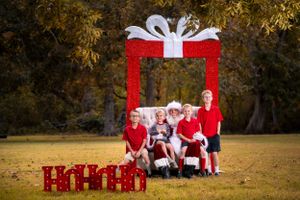 Festive holiday outdoor photo session with red and white decorations featuring large gift box prop and packages.