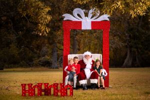 Christmas photo setup with large red present frame and decorative boxes on autumn grass.