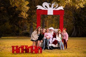 Outdoor holiday portrait setting with decorative red gift frame and seasonal props.