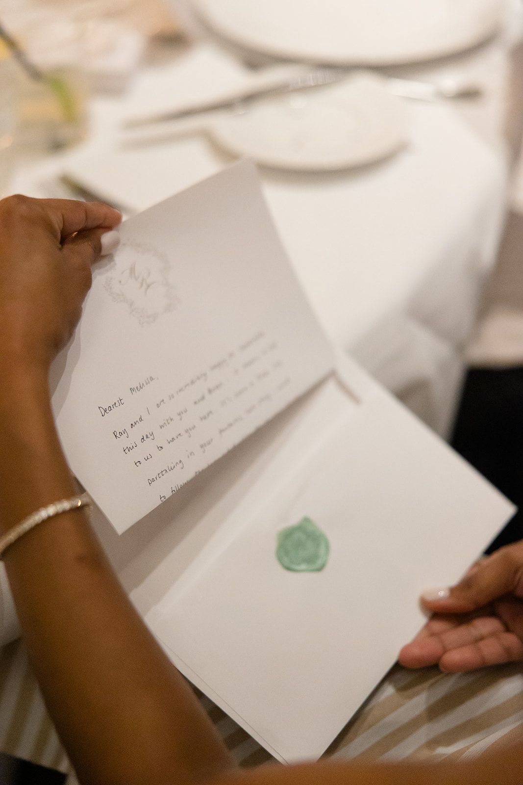 Hands holding an opened greeting card with handwritten text and a small green seal or embellishment inside.
