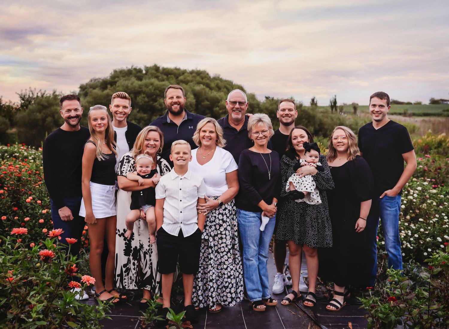 Large family group photo outdoors in a flower garden at sunset.