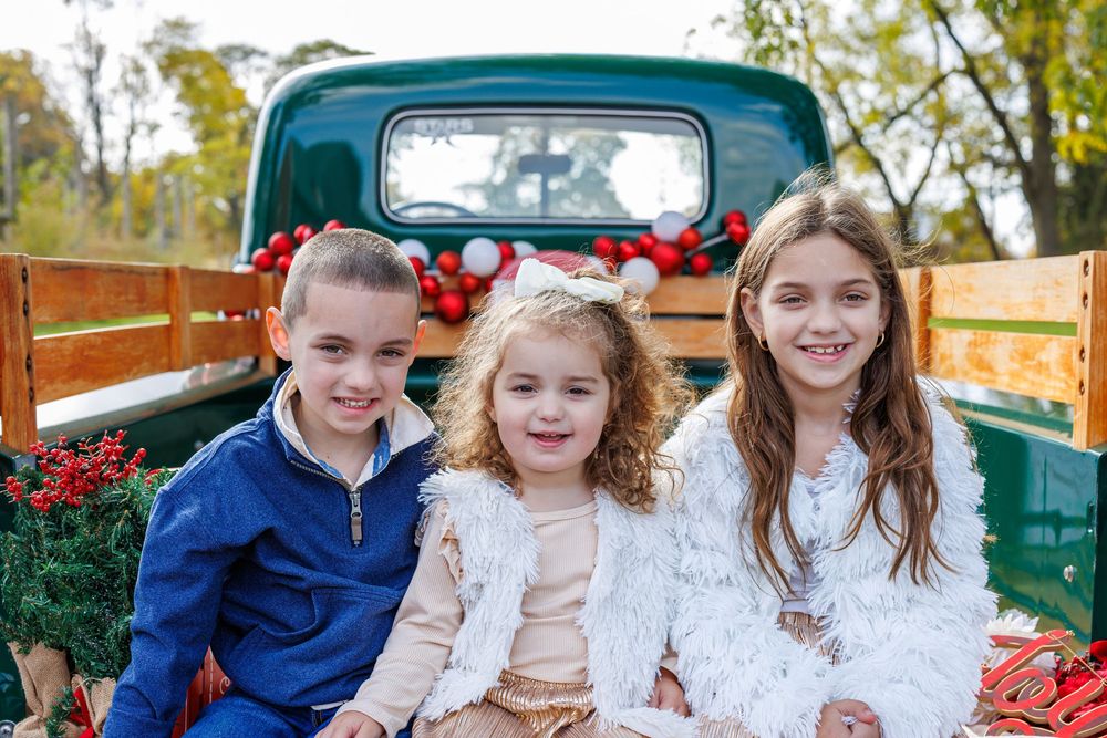 Children sitting together on vintage green truck with holiday decorations.