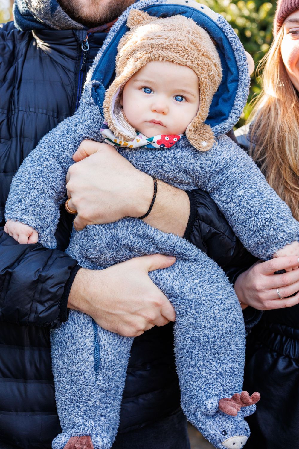 Baby wearing cozy blue winter outfit being held during photo session.