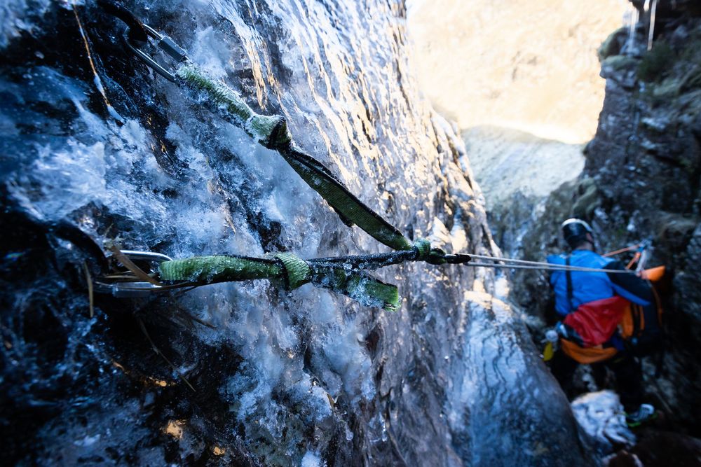 A canyoneer rigs an abseil with frozen anchors embedded in ice