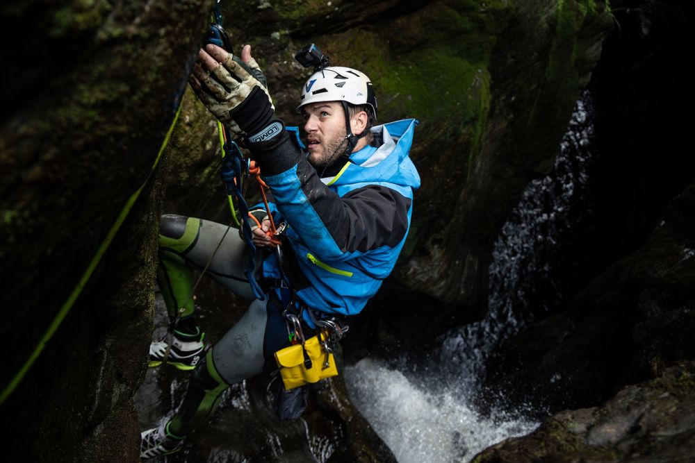 A person in blue gear rappels down a waterfall during a canyoning adventure in a dark rocky gorge.