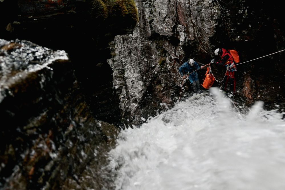 An filmmaker captures a canyoneer abseiling within a deep gorge