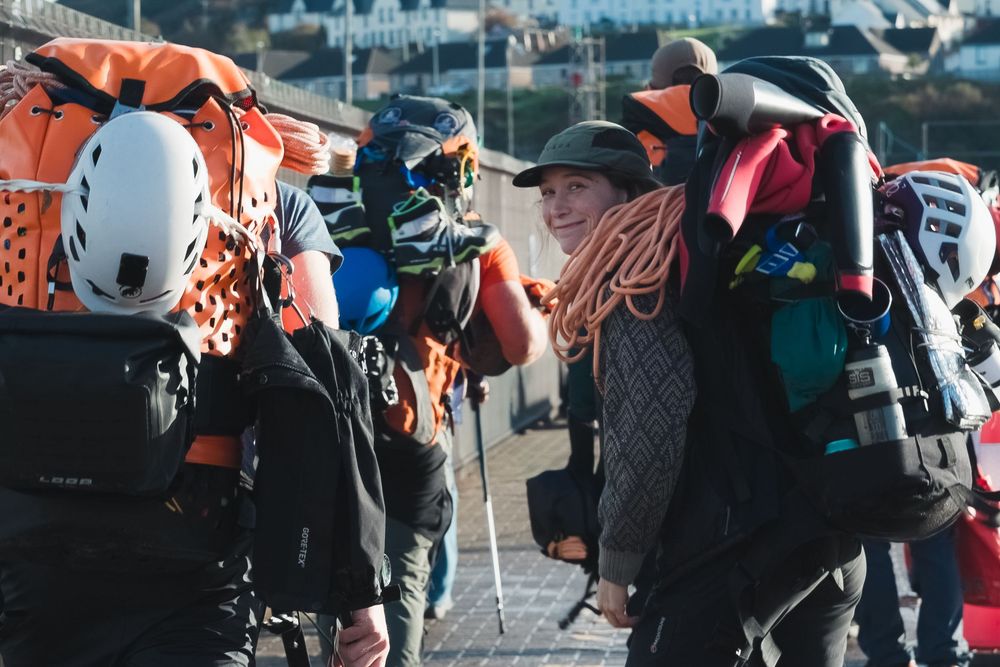 Group of canyoneers with large backpacks and ropes walk toward a ferry