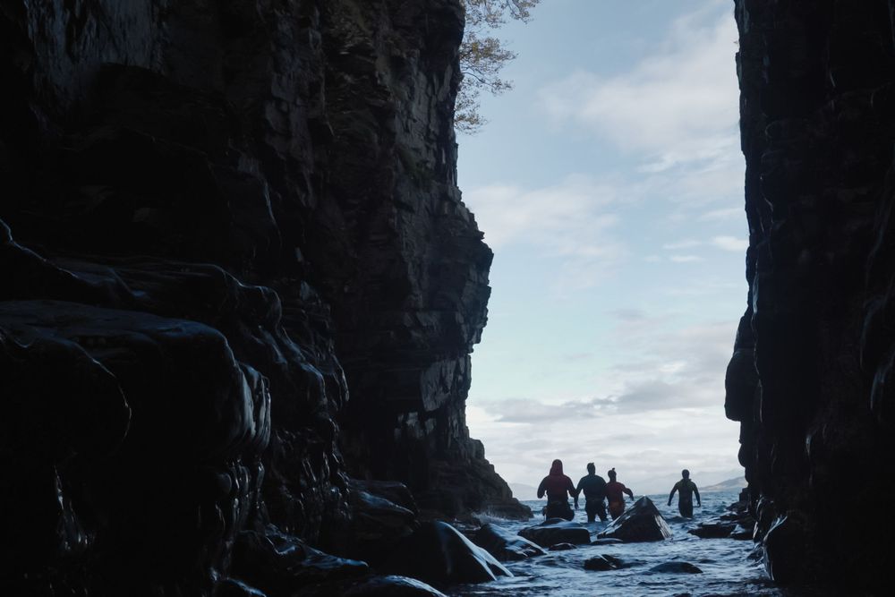Canyoneers walk out from a deep dark gorge into an open blue sea