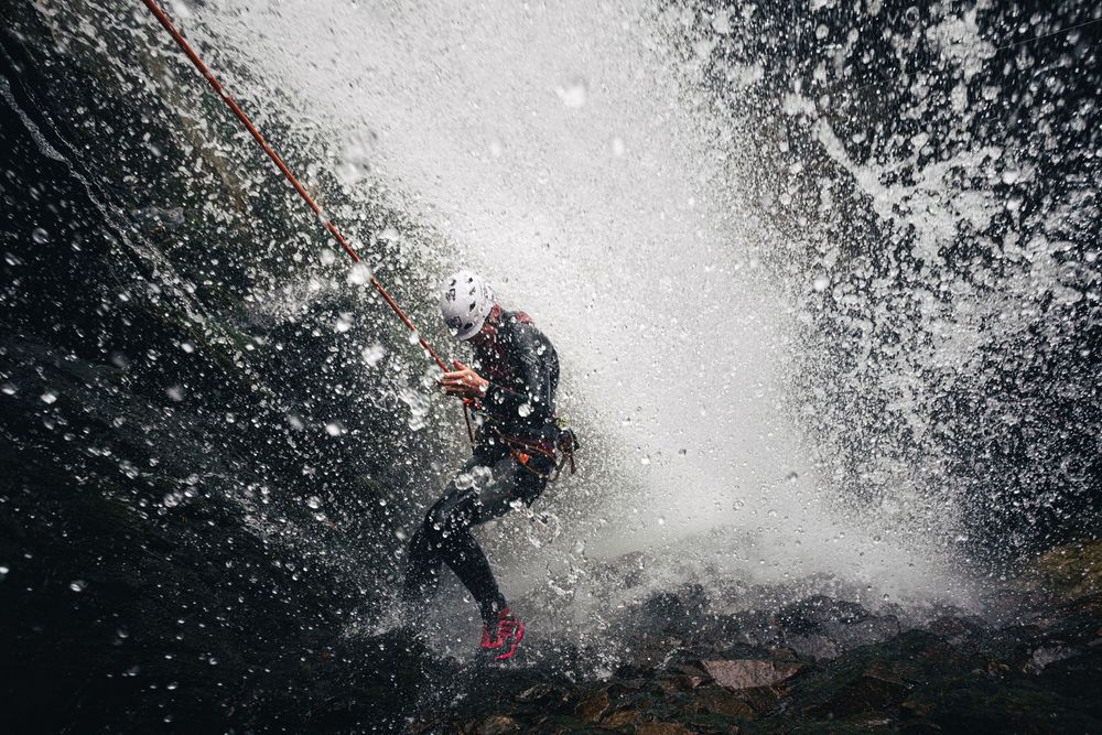 A canyoneer abseils behind the curtain of a large waterfall