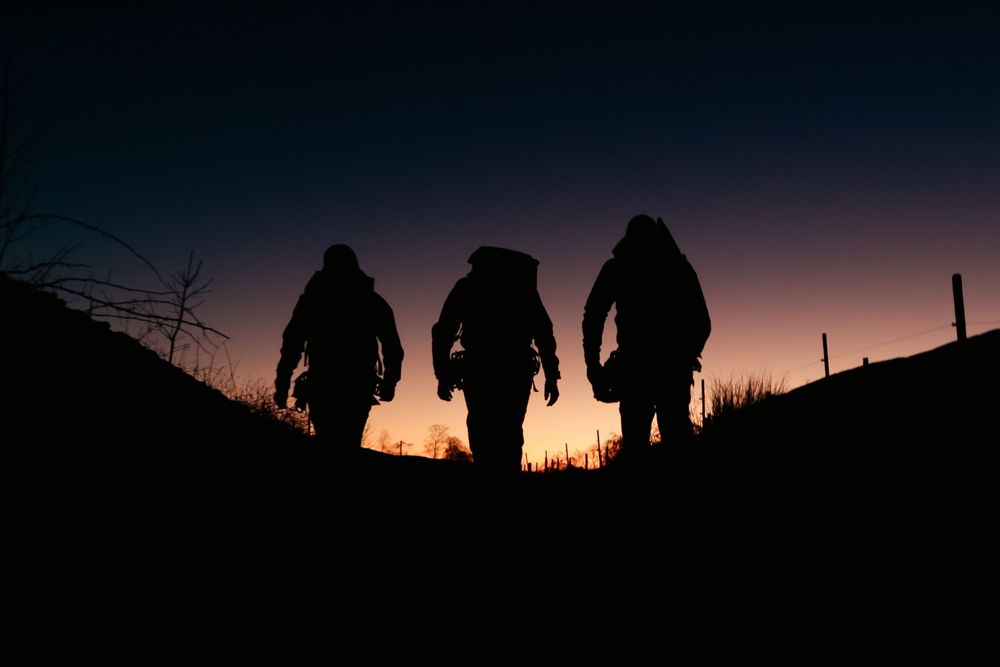 Silhouettes of people walking against a dramatic sunset sky with trees in the background.