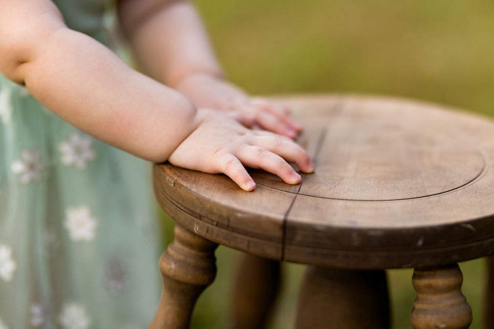 Close-up view of hands touching a rustic wooden stool surface in natural outdoor lighting.