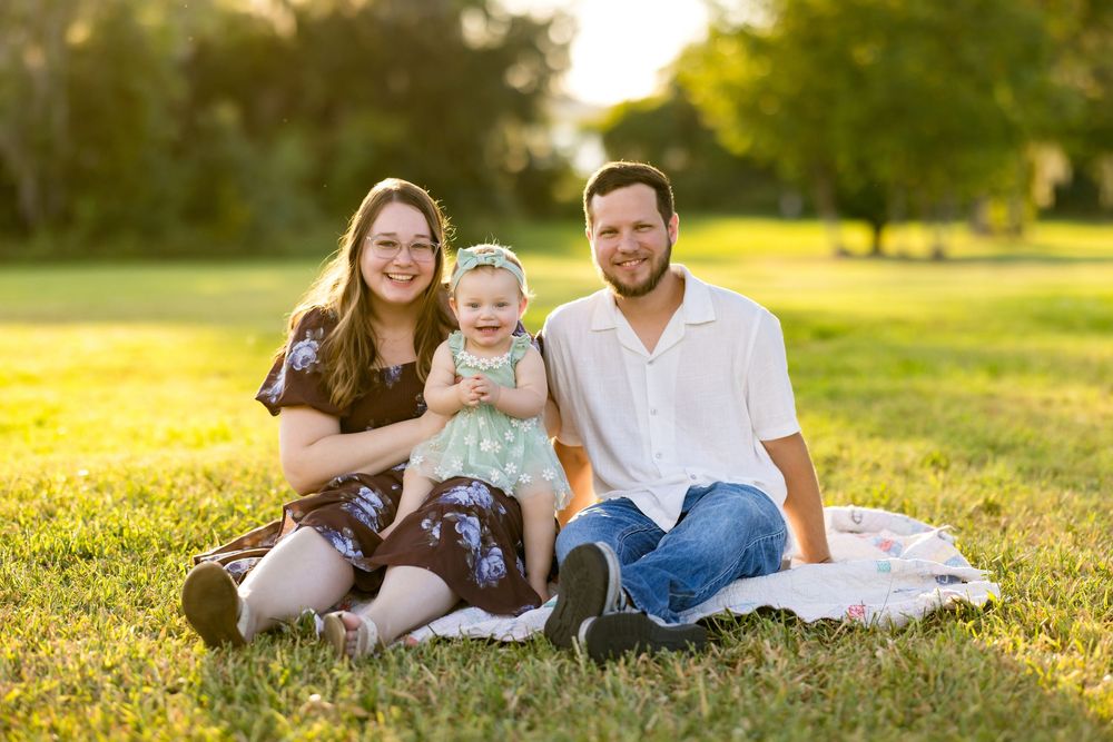 A family lounges together on green grass during a warm sunset in a park setting.