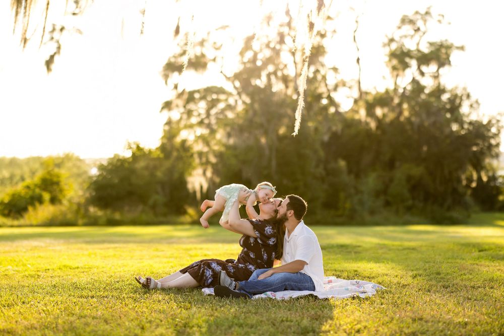 Two people sit on a blanket in a sunny field at golden hour with their dog, enjoying a peaceful moment together.