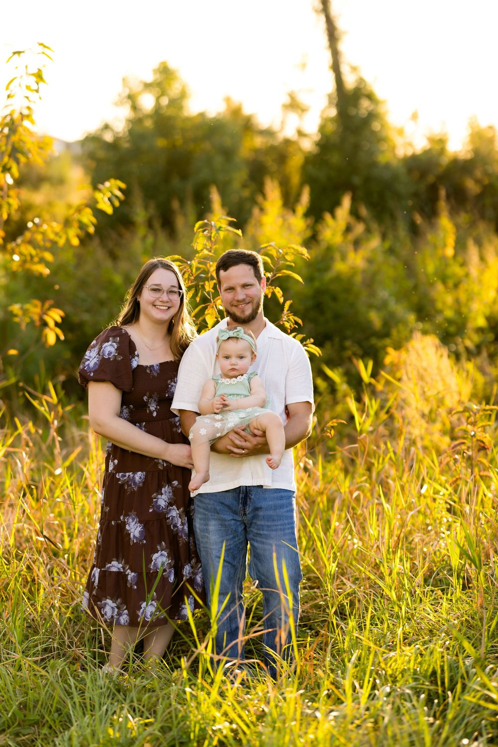 A family enjoys a tender moment together in a sunlit meadow with tall golden grass at sunset.