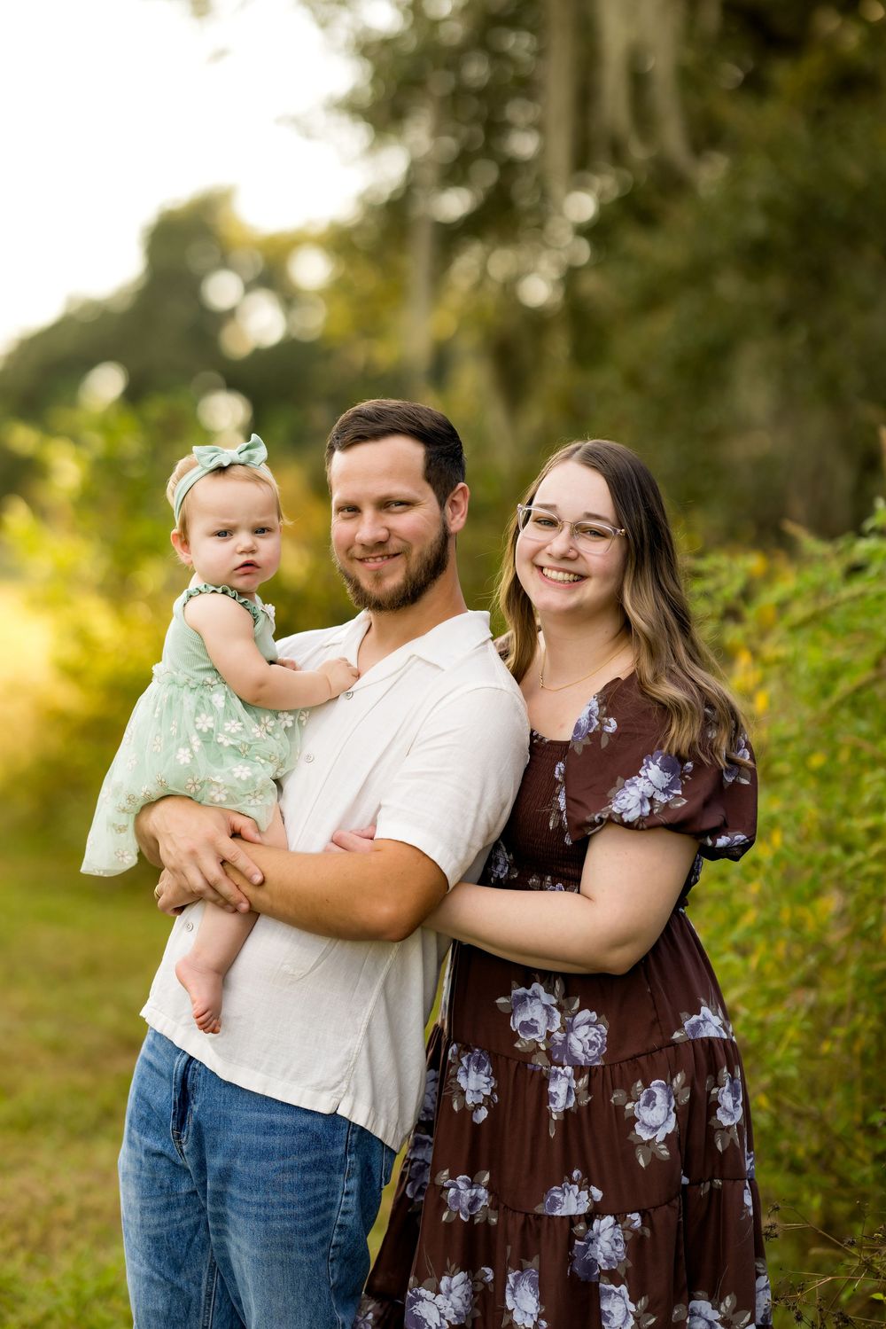 Family portrait session in a natural outdoor setting with warm golden sunlight filtering through trees in the background.