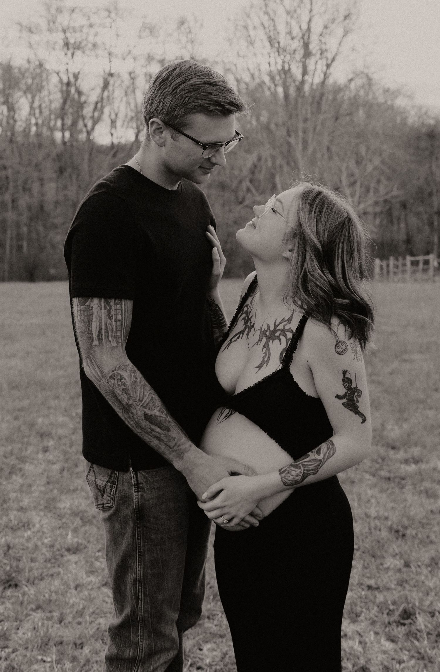 Black and white portrait of a couple with tattoos embracing outdoors.