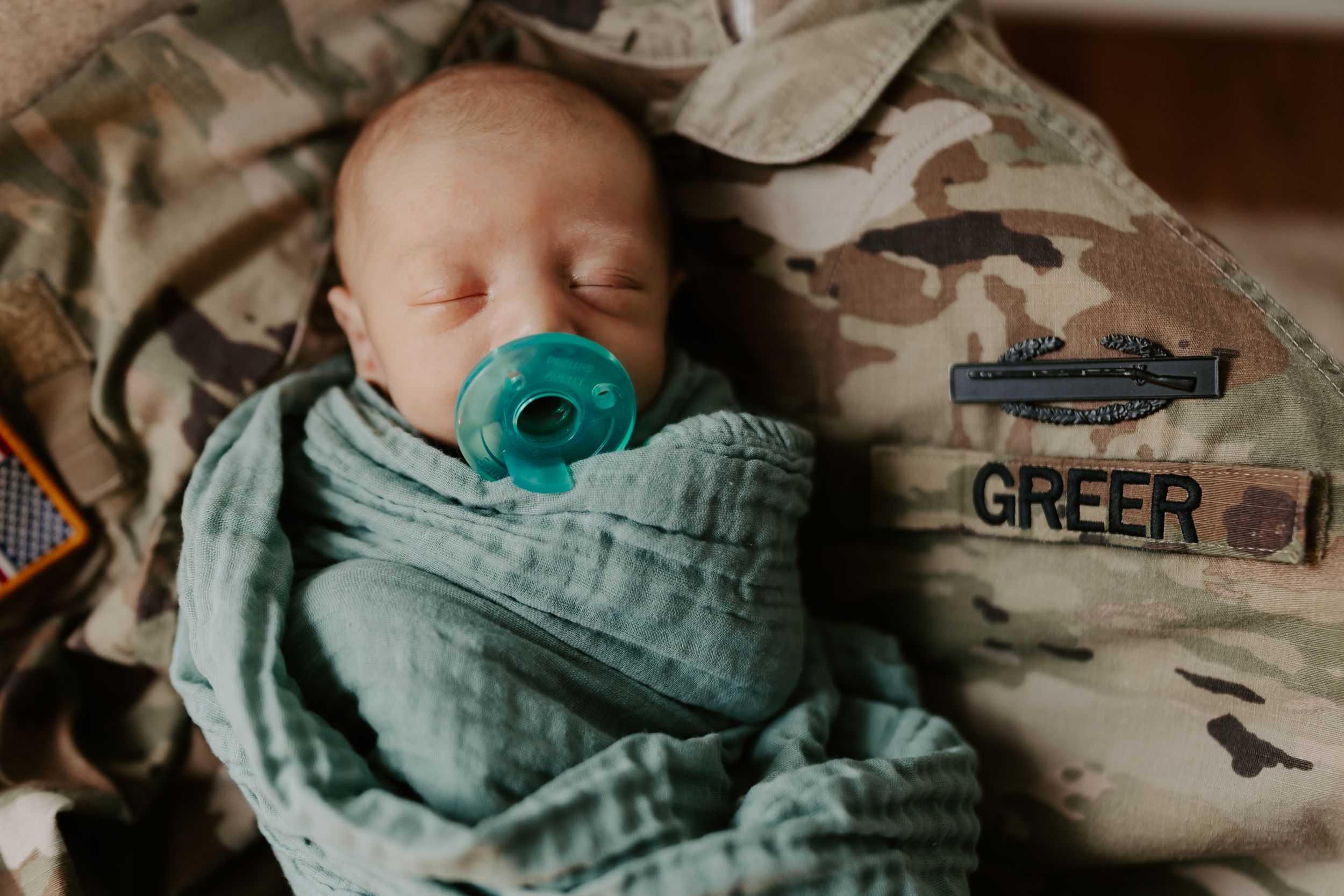 Newborn baby wrapped in soft teal swaddle blanket against neutral background.