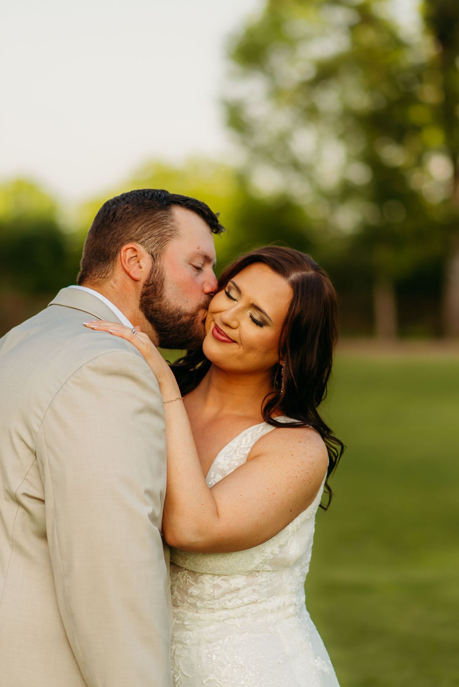 A romantic wedding couple shares an intimate moment outdoors in a natural setting during golden hour.