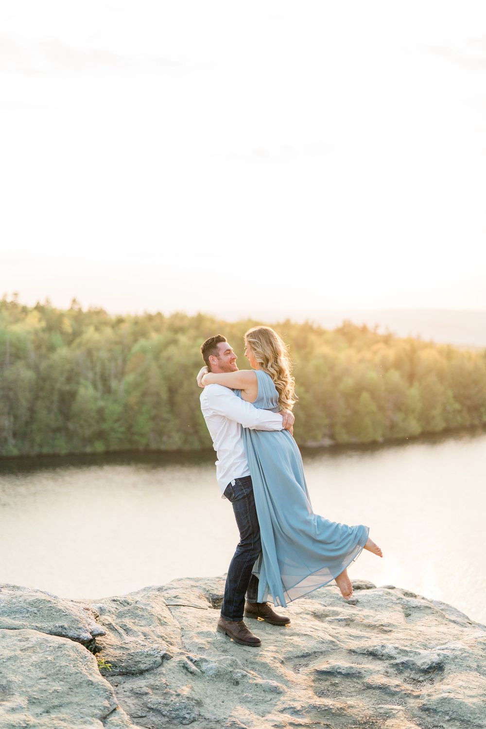 Couple dancing on rocky cliffs during golden hour sunset engagement session.