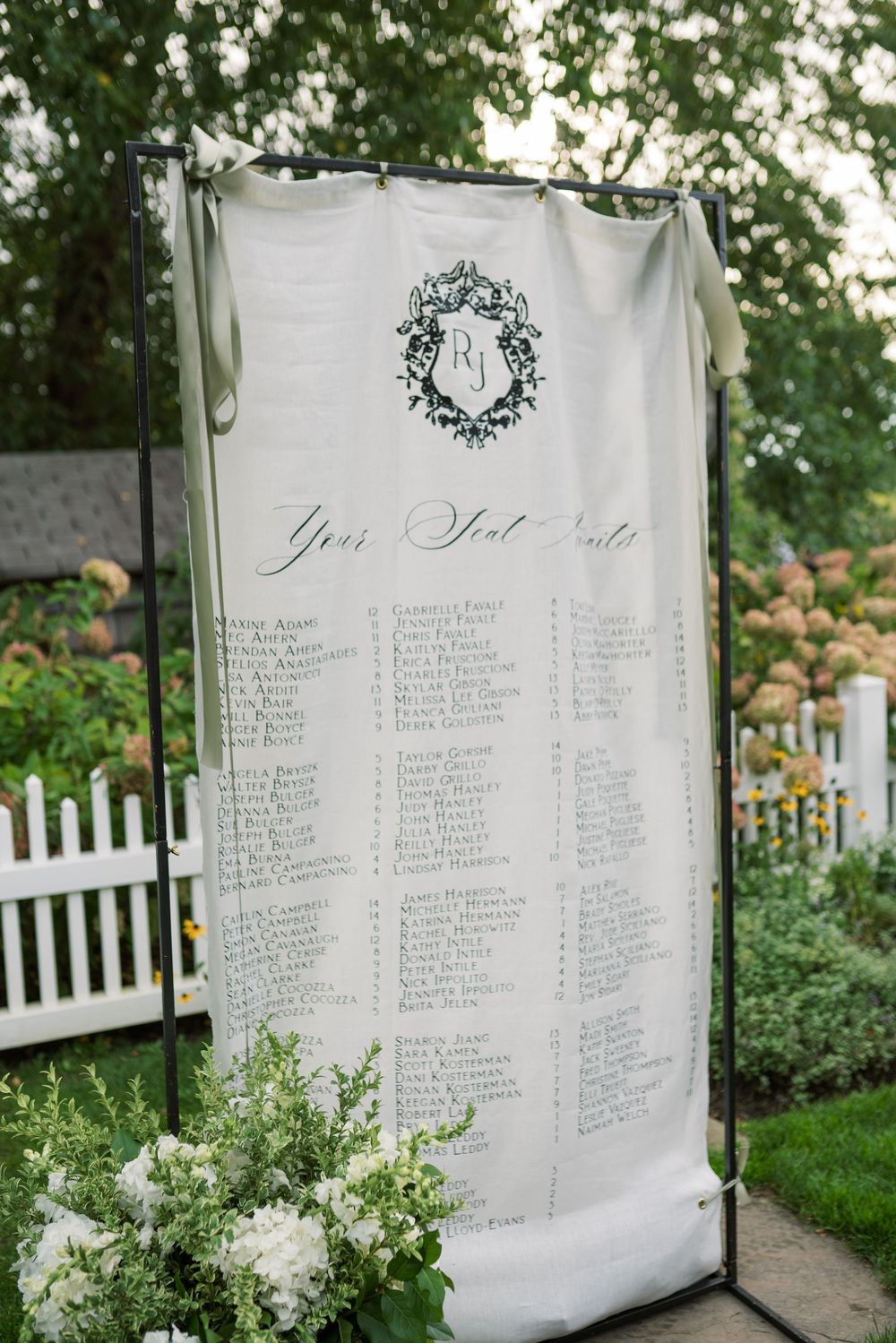 Elegant white seating chart display with floral decorations at an outdoor wedding venue.