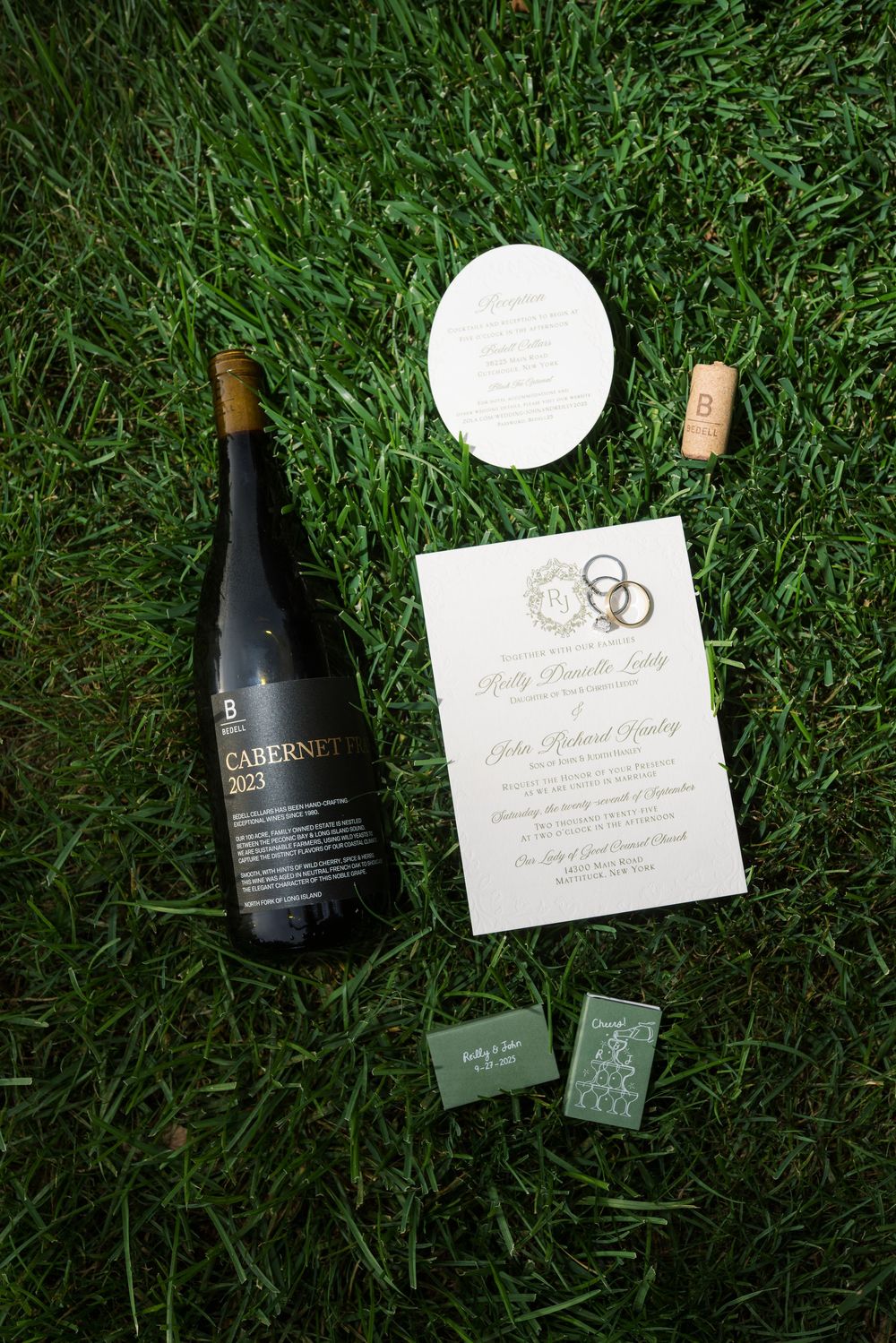 Wedding invitation and wine bottles arranged artistically on green grass.