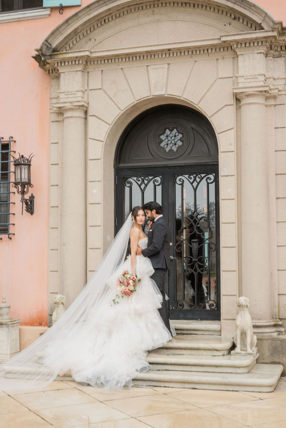 Grand entrance of a luxury venue with ornate stone archway and pink stucco walls.