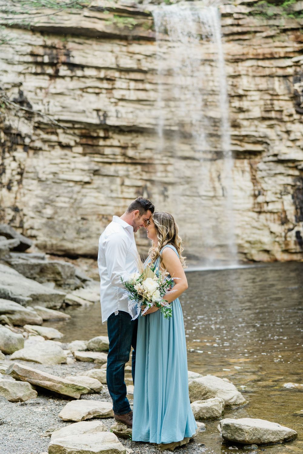 Couple in formal attire sharing an intimate moment by a limestone waterfall.