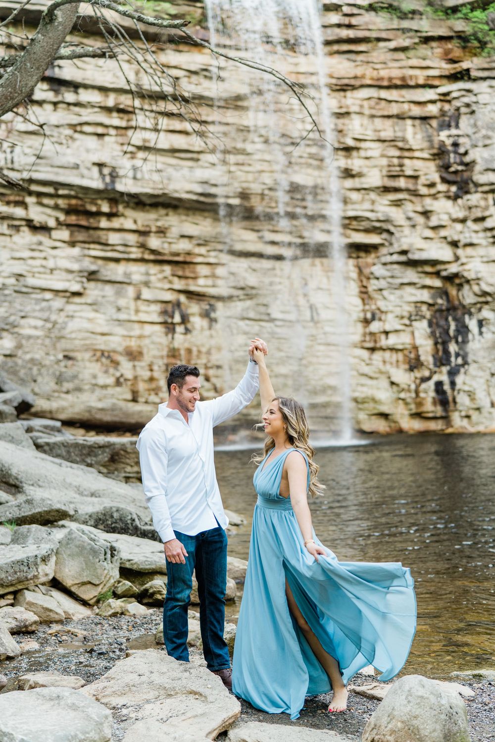 Couple in blue dress and white shirt dancing near a cascading waterfall.