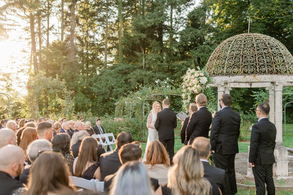 Wedding ceremony guests seated outdoors under ornate gazebo during golden hour.