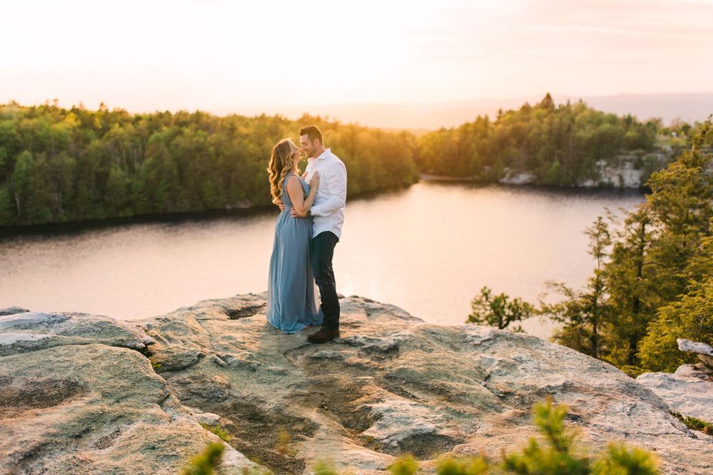 Romantic sunset engagement photo session on a rocky cliff overlooking a lake.