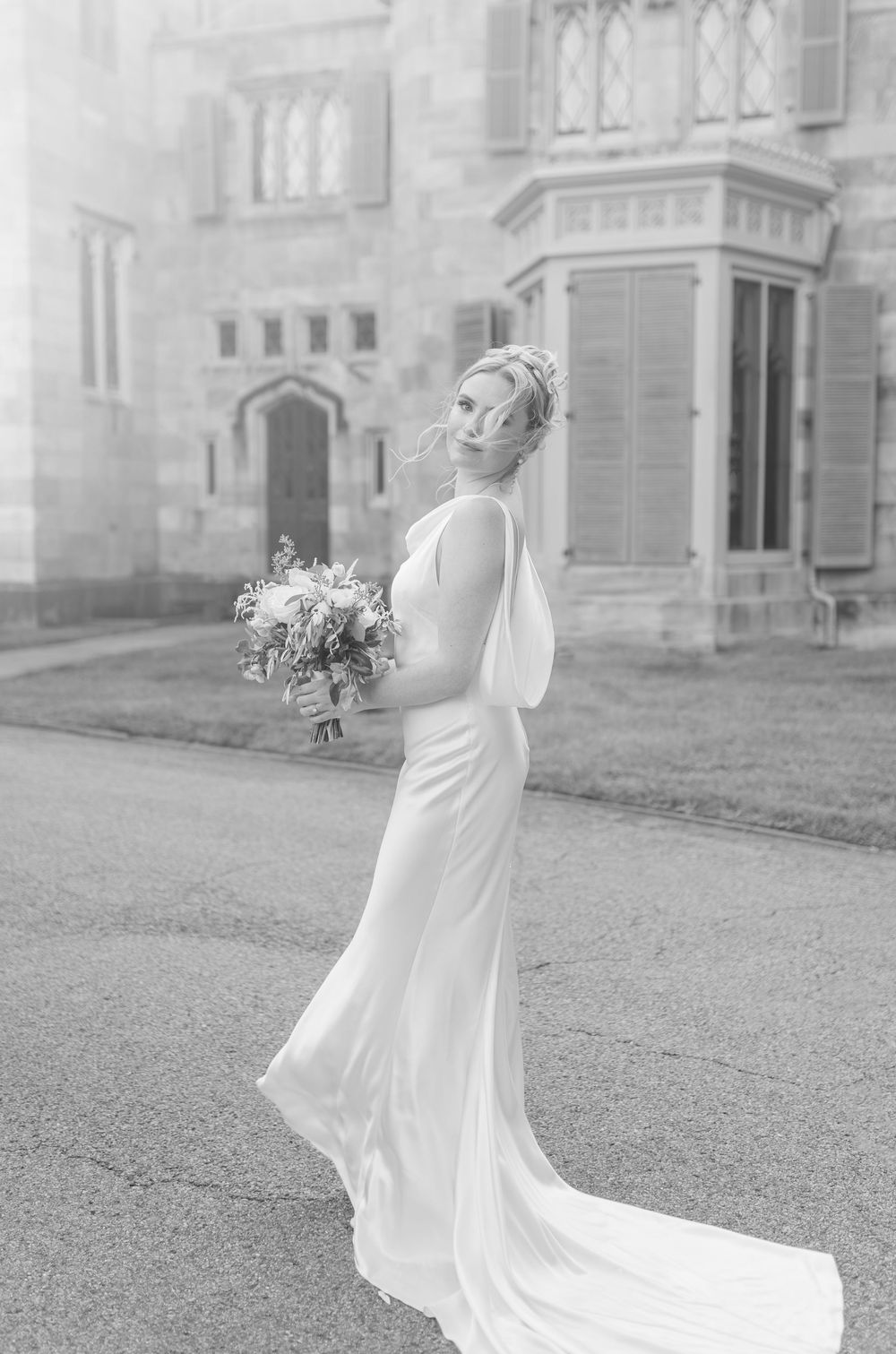 Elegant white wedding dress flowing in motion against a historic stone building backdrop.