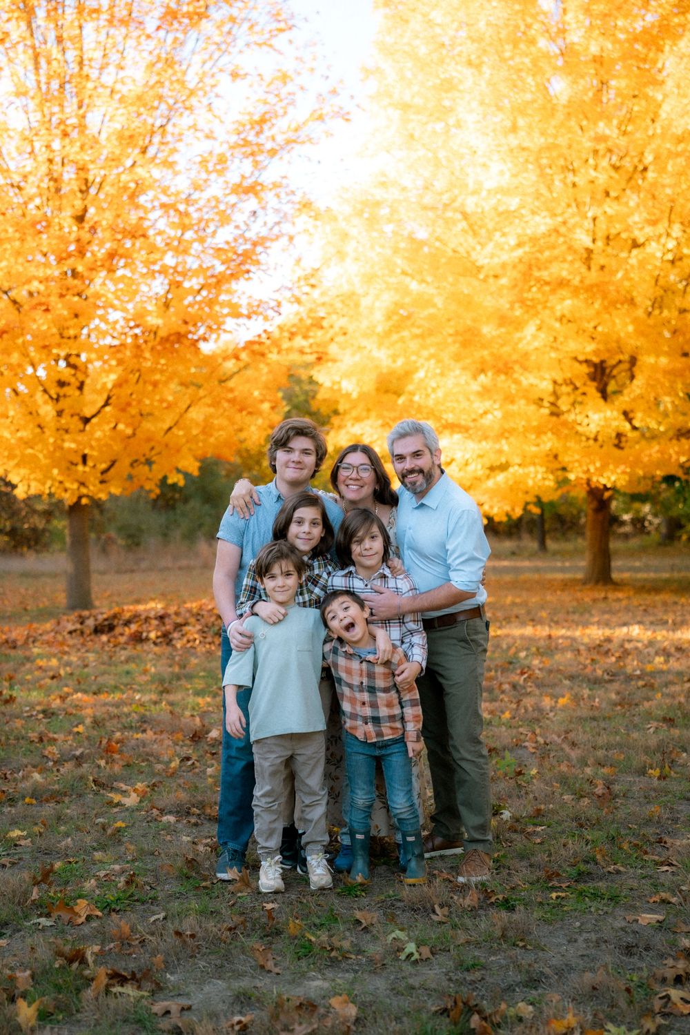 A family poses together outdoors on an autumn day with golden yellow trees creating a warm backdrop.