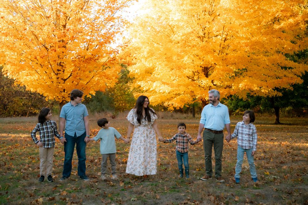 A group walks together through a golden autumn forest during sunset as fallen leaves cover the ground.