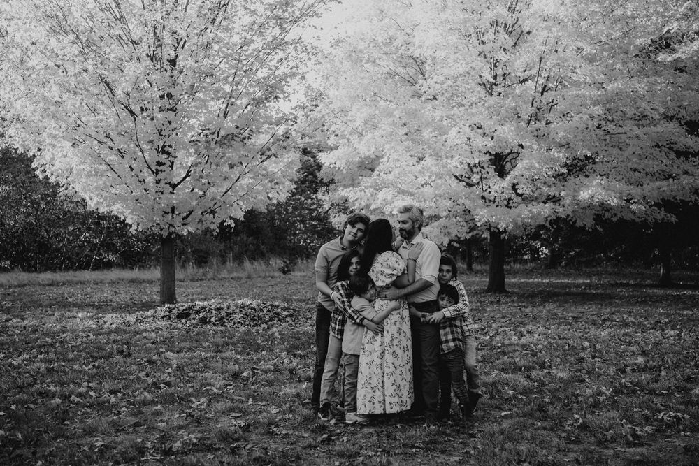 A group of people embrace in a loving hug under blooming cherry blossom trees in black and white photography.