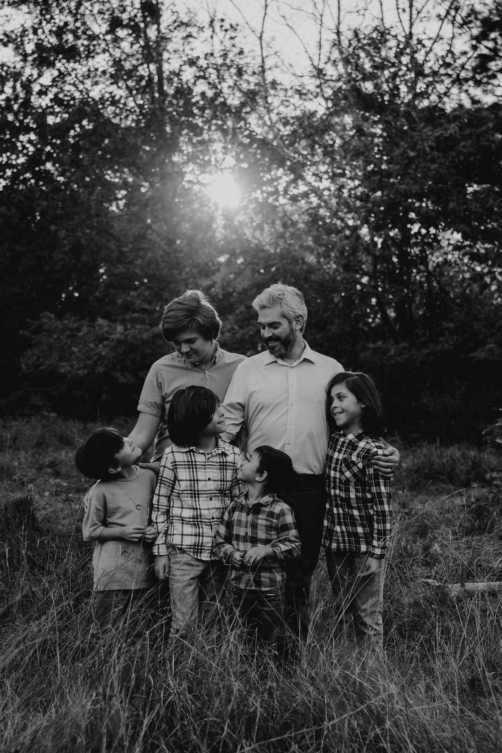 A group stands together in tall grass at sunset creating a silhouetted scene in black and white.