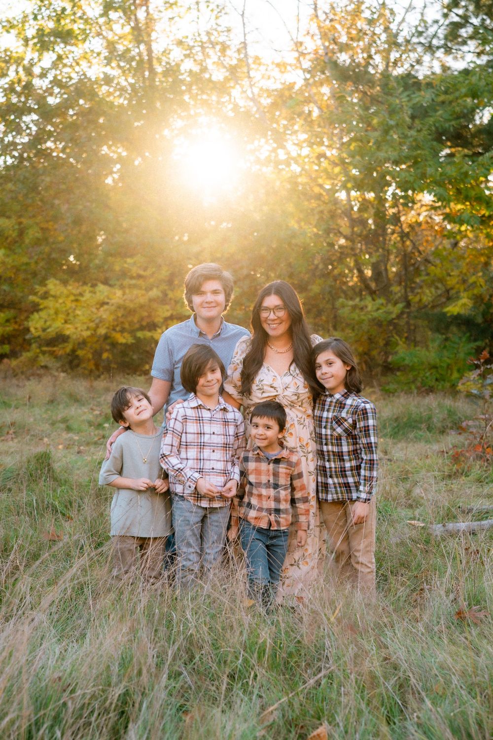 Group standing together in tall grass field at sunset with warm golden light filtering through trees.