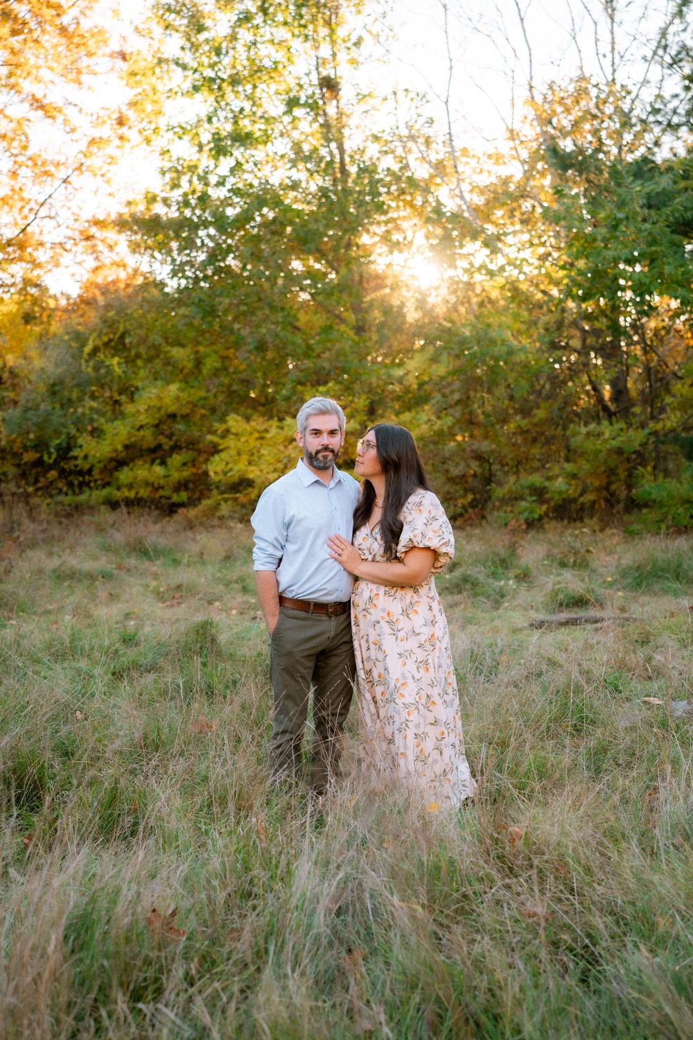 A couple shares an intimate moment in a golden sunlit meadow with tall grass during sunset.