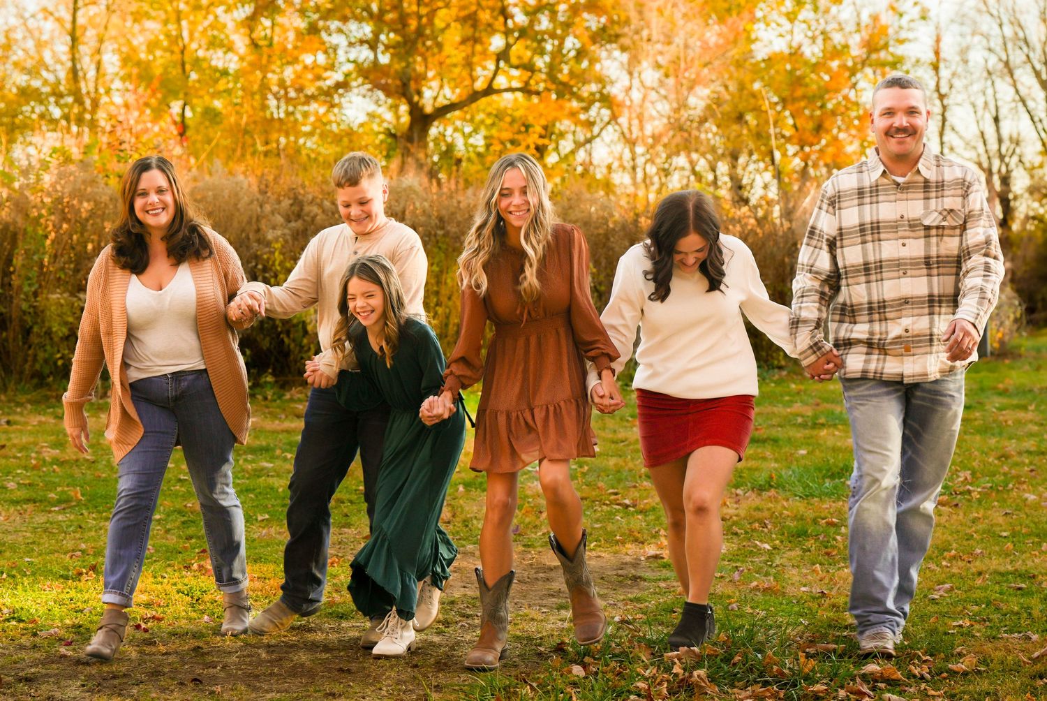 Group of people playfully walking together on an autumn day with golden trees in the background. Quad Cities Family Photography