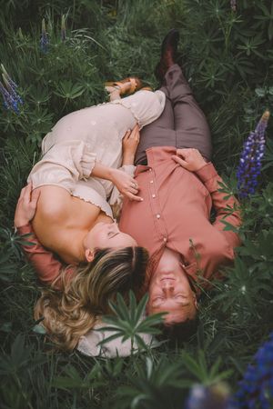A couple lies peacefully in a garden surrounded by lush greenery and blooming purple lupine flowers during their Seattle couples photoshoot