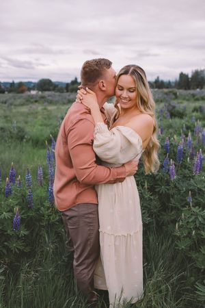 A couple shares intimate moments in a field of purple lupine flowers at sunset during their Seattle, WA engagement photoshoot