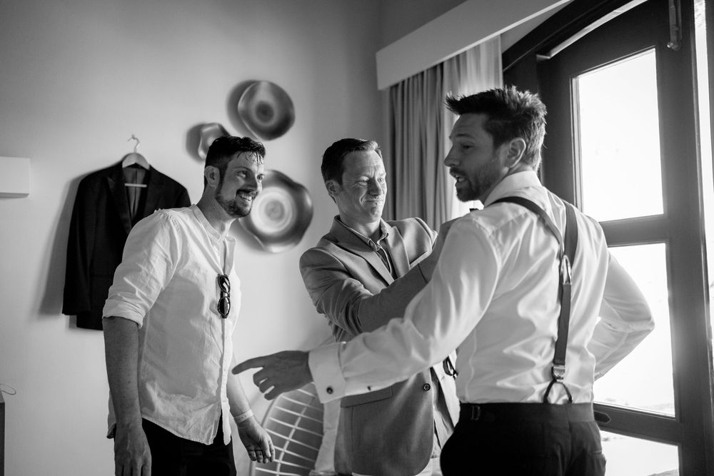 Groomsmen getting ready and helping each other prepare for a wedding ceremony in black and white.