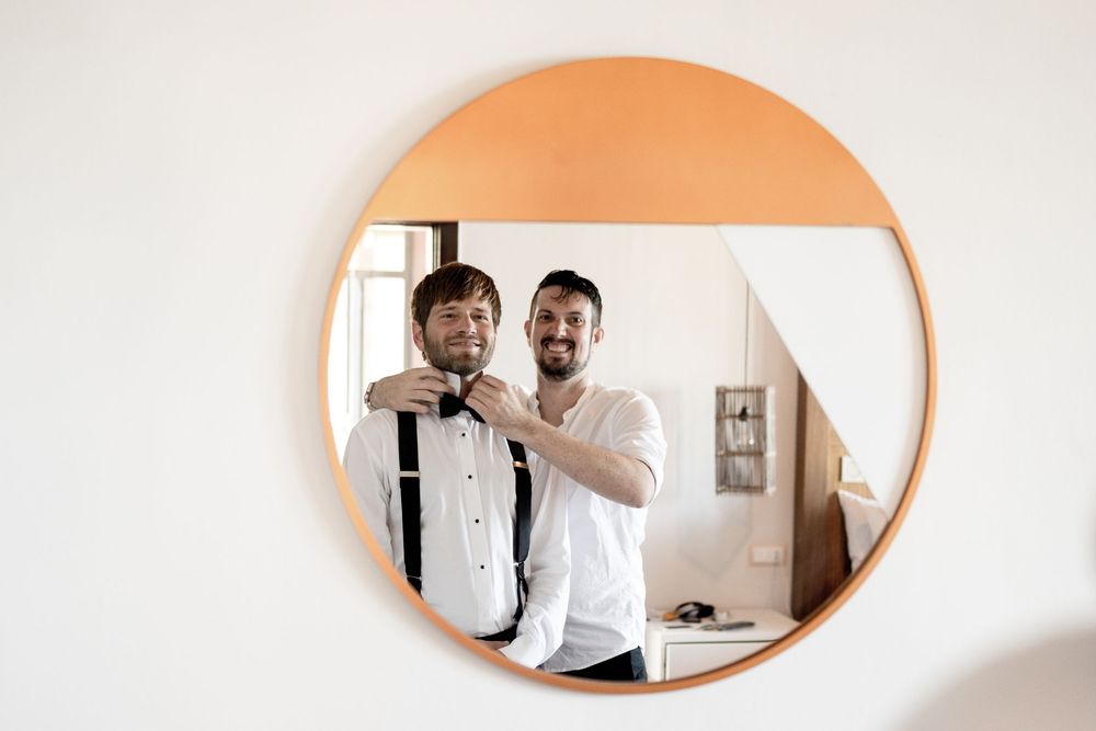 Two people in white shirts smile while working together at a desk with laptops and papers.