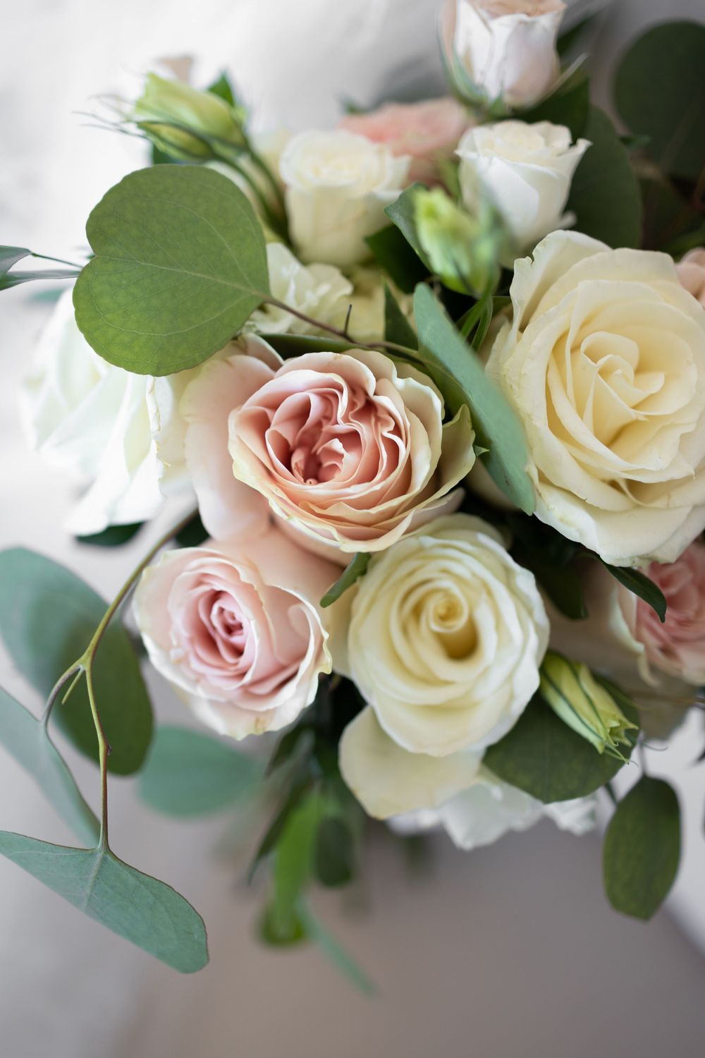 Delicate pink and white roses with eucalyptus leaves in an elegant wedding bouquet arrangement.