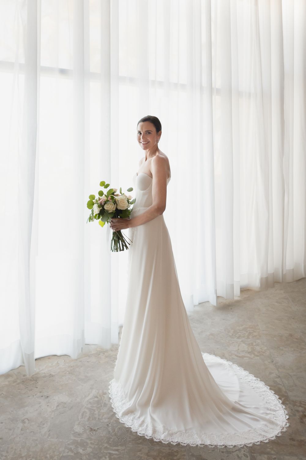 Elegant bridal portrait series against white curtains showing the flowing train of a white wedding gown.
