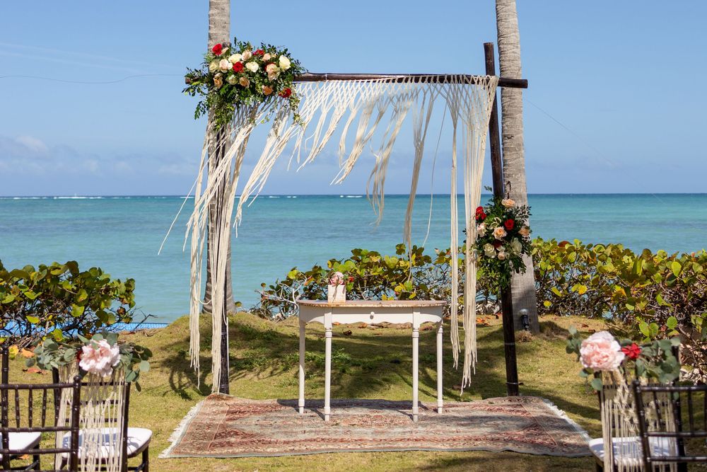 Tropical beach wedding ceremony setup with bamboo arch decorated with flowers and white fabric overlooking turquoise ocean.