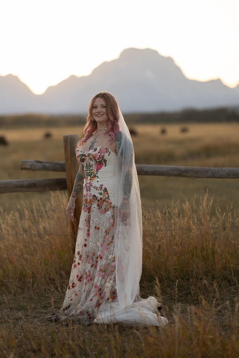 A floral dress and veil create an ethereal silhouette against a golden field at sunset.