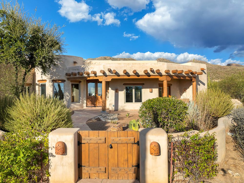 Southwestern style adobe home exterior with wooden gates and desert landscaping under blue skies.